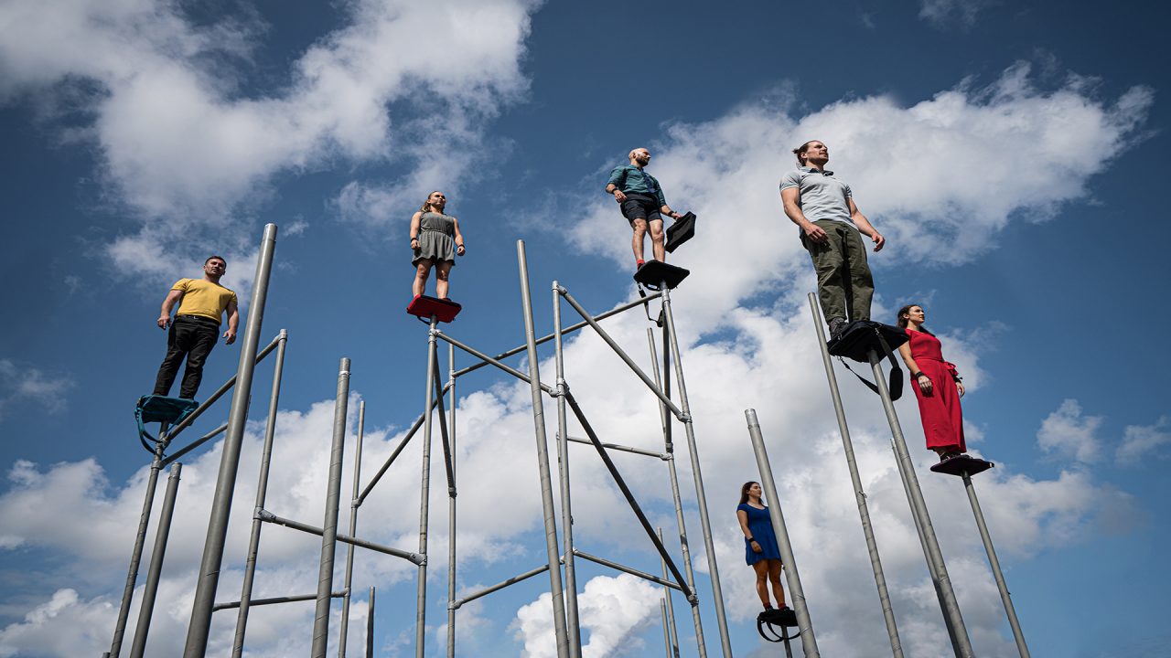 dancers balancing on top of a set made of tall poles