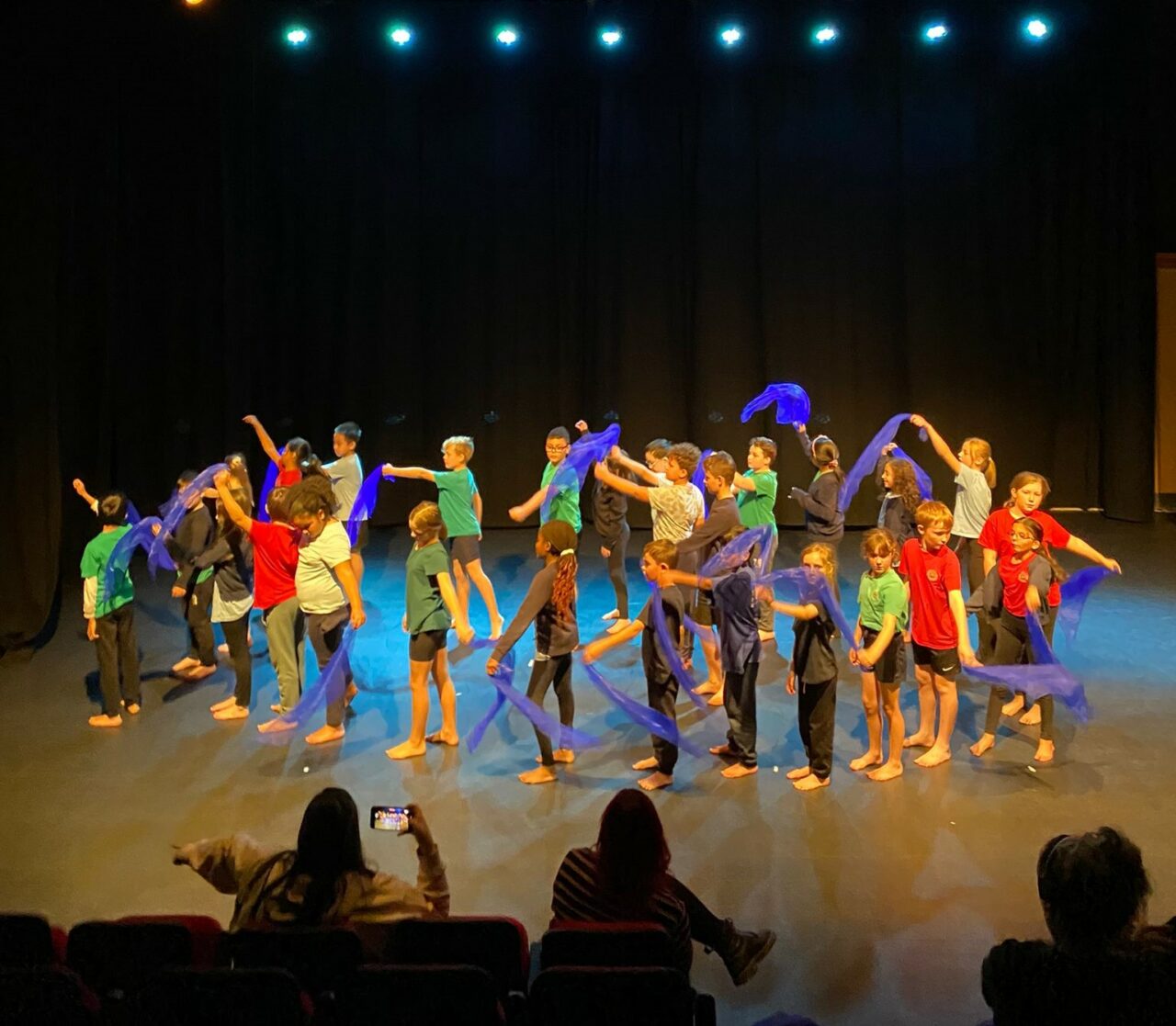Children in colourful t-shirts performing on stage waving blue scarves
