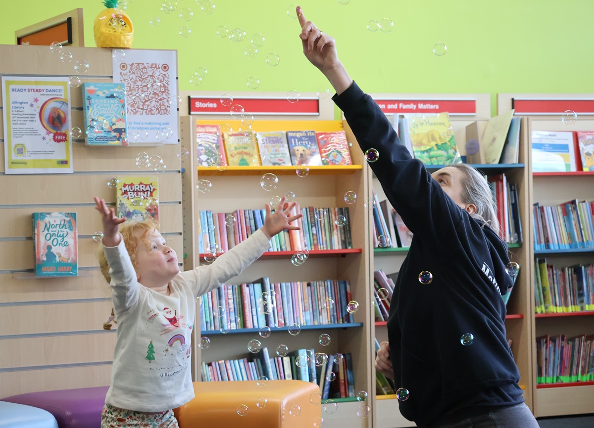 young child reaches arms up to catch bubbles
